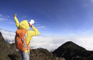young woman backpacker shouting with loudspeaker on beautiful mountain peak
